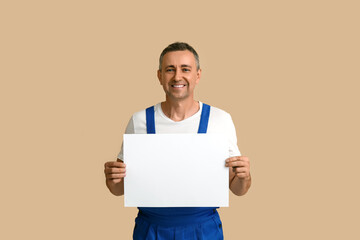 Portrait of male mechanic with blank poster on beige background