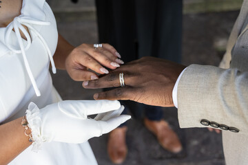 Newly married bride places wedding ring on the black finger of her husband hand during ceremony