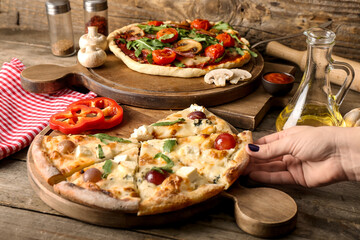 Female hand with delicious pizzas, ingredients and napkin on wooden background