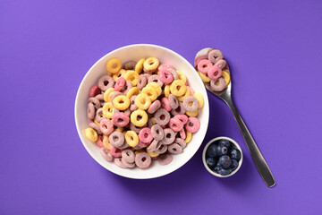 Bowls with colorful sweet cereal rings and blueberries on purple background