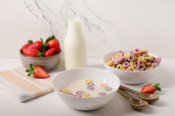 Bowls of colorful sweet cereal rings with milk and strawberries on white background