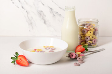 Bowl of colorful sweet cereal rings with milk and cut strawberry on white background