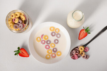 Bowl of colorful sweet cereal rings with milk and cut strawberry on white background