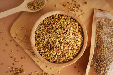 Bowl and pack with raw buckwheat grains on beige background, closeup
