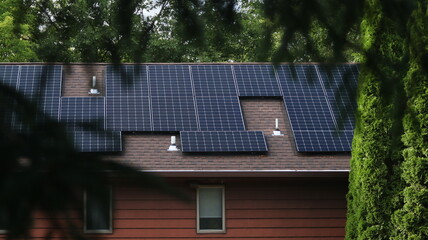 Solar photovoltaic panels on the roof of a red house framed by a foreground of green trees. Solar Panel Module technology creating renewable energy in New Jersey.