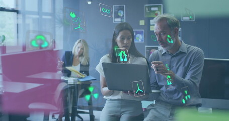Image of ecology icons over diverse colleagues using laptop and discussing work in office