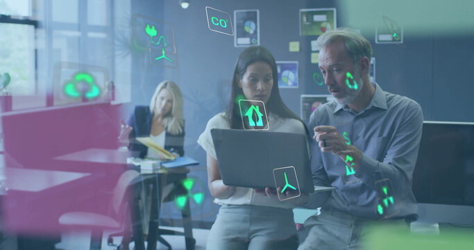 Image of ecology icons over diverse colleagues using laptop and discussing work in office - Powered by Adobe