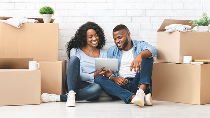 Shopping online. Young african girl showing her man ideas for interior in new house, using digital tablet, panorama with copy space © Prostock-studio