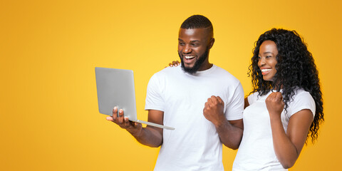 A man and woman are both smiling and looking at a laptop screen with excitement.
