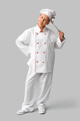 Portrait of thoughtful teenage chef with ladle on grey background