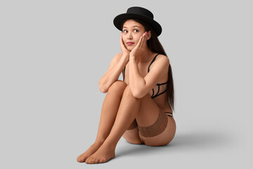 Beautiful woman wearing hat, underwear and stockings on light background
