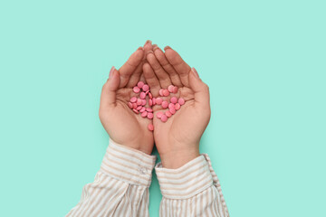 Female hands with pink pills on turquoise background