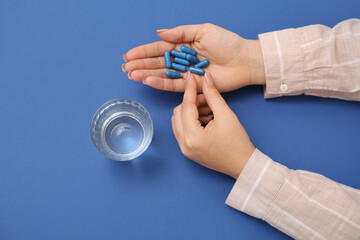 Female hands with pills and glass of water on blue background