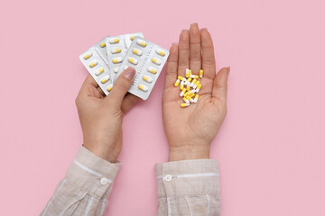 Female hands with pills in blister packs on pink background