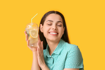 Beautiful young happy woman with cup of fresh lemonade on yellow background