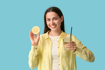 Beautiful young happy woman with lemon half and glass of fresh lemonade on blue background