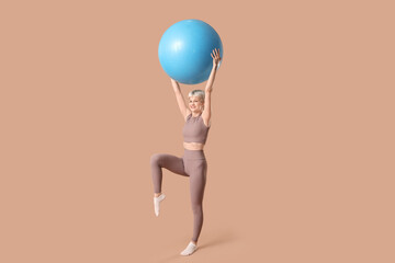 Sporty young woman  training with fitball on beige background