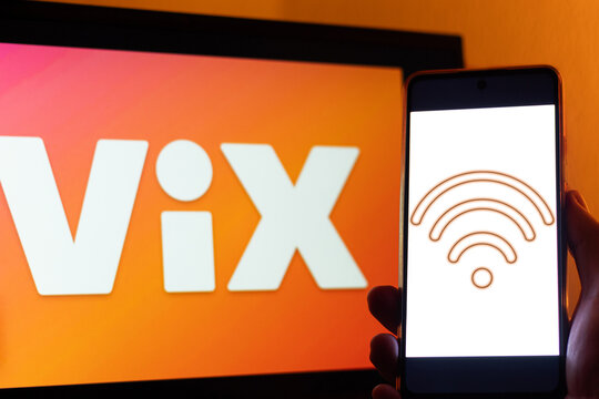 A hand holds a smartphone with a blank screen with a connectivity icon in front of a larger screen with the logo of Vix, a streaming platform for movies, series, soap operas and sports.