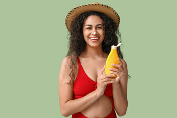 Beautiful young happy African-American woman with bottle of sunscreen cream on green background