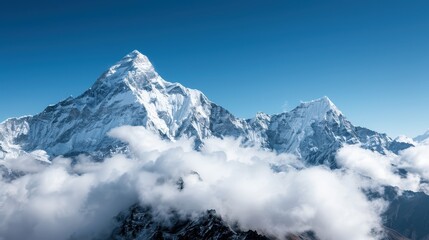 Majestic snow-covered mountain peaks rise above the clouds, displaying their grandeur against a clear blue sky, capturing the serene and awe-inspiring beauty of nature.