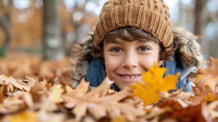 Fototapeta premium A young child smiling warmly while surrounded by autumn leaves, dressed in cozy, warm clothing and a knitted hat, epitomizing the essence of a joyful autumn day.