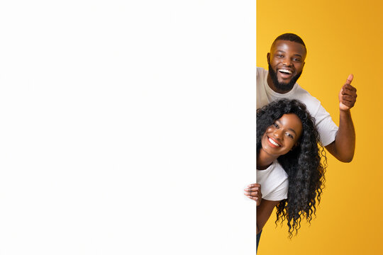 A couple smiles and gives a thumbs up as they peek around a corner against a bright yellow background.