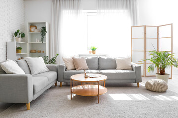 Cozy sofa with cushions, coffee table and folding screen in interior of living room