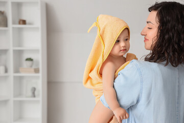 Mother with her little baby in towel after bathing at home, back view