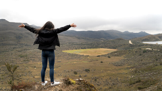 young latina woman and traveler enjoying nature with a frailejon (espeletia) valley and lagoon. Wearing non sports clothes. She is back with open arms