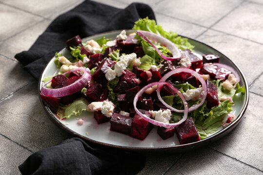 Plate of fresh salad with beet and slices of red onion on grey tile background