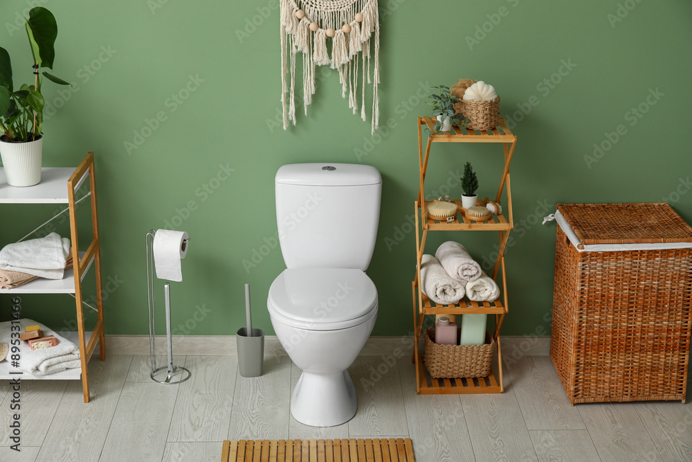 Sticker Toilet bowl, shelving unit, paper holder and laundry basket near green wall in restroom