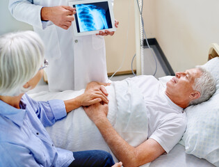 Doctor, senior and patient with xray on tablet for consultation with screen for evaluation of joint condition and arthritis. Old man, wife and support in hospital for mri on shoulder and bursitis.