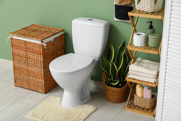 Interior of restroom with toilet bowl, shelving unit, laundry basket and organizer near green wall