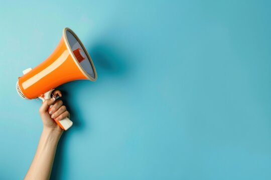 Hand holding an orange megaphone against a blue background, symbolizing communication and announcement.