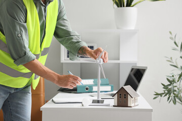 Male engineer with wind turbine and house model working at table in office, closeup