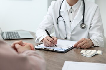 Doctor writing prescription for patient at wooden table in clinic, closeup