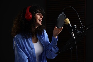 Vocalist with headphones singing into microphone in professional record studio