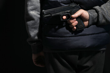 Man hiding gun behind his back on black background, closeup. Armed robbery
