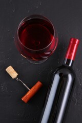 Corkscrew, glass of wine and bottle on black table, flat lay