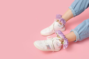Legs of young woman in sneakers with lilac eustoma flowers on pink background