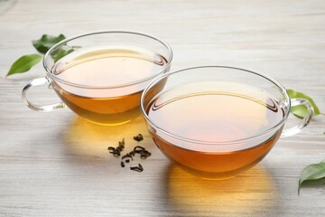 Refreshing green tea in cups and leaves on light wooden table, closeup