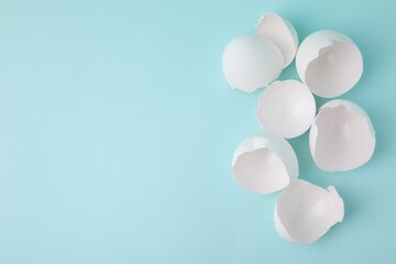 Broken eggshells on light blue background, top view. Space for text