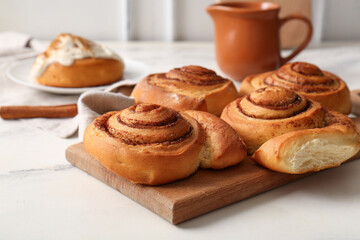 Wooden board with sweet cinnamon rolls on white background