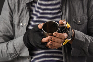 Mature homeless man with cup asking for money on dark background, closeup