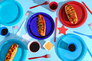 Tasty hot dogs with USA flags, cola and plastic plates on blue background. American Independence Day celebration