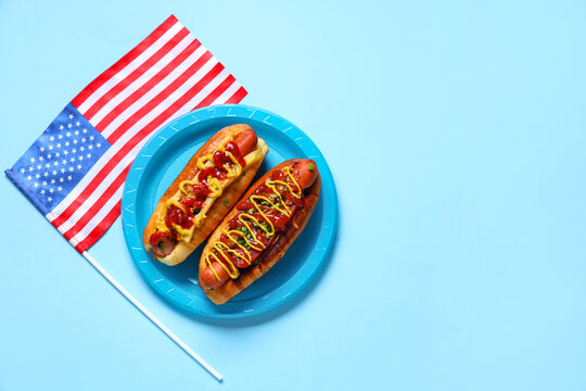 Plate with tasty hot dogs and USA flag on blue background. American Independence Day celebration