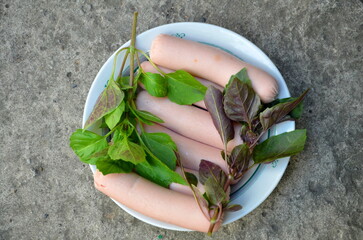 Six sausages on a plate with the addition of green and brown basil.