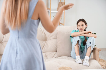 Fototapeta premium Sad teenage girl sitting on sofa with her arguing mother at home. Family difficulties concept