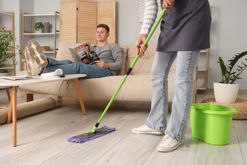 Lazy husband reading magazine while his wife mopping at home