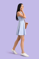 Young woman talking by mobile phone on lilac background